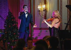 Item is a photograph closeup of two performers on stage during the Christmas in the City fundraising event. One performer is singing and the other is playing a violin. This event was held in a ballroom at the Fairmont Hotel in Vancouver.