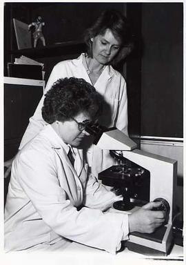 Two Instructors in lab coats looking in a microscope