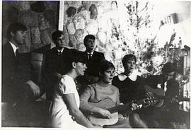 Mixed ensemble singing and playing guitar near a Christmas tree