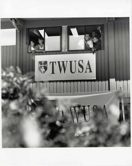 Five students at a window with a large sign reading TWUSA beneath it