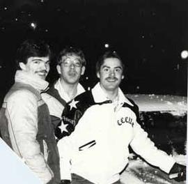 Three male students outside on a snowy evening on campus